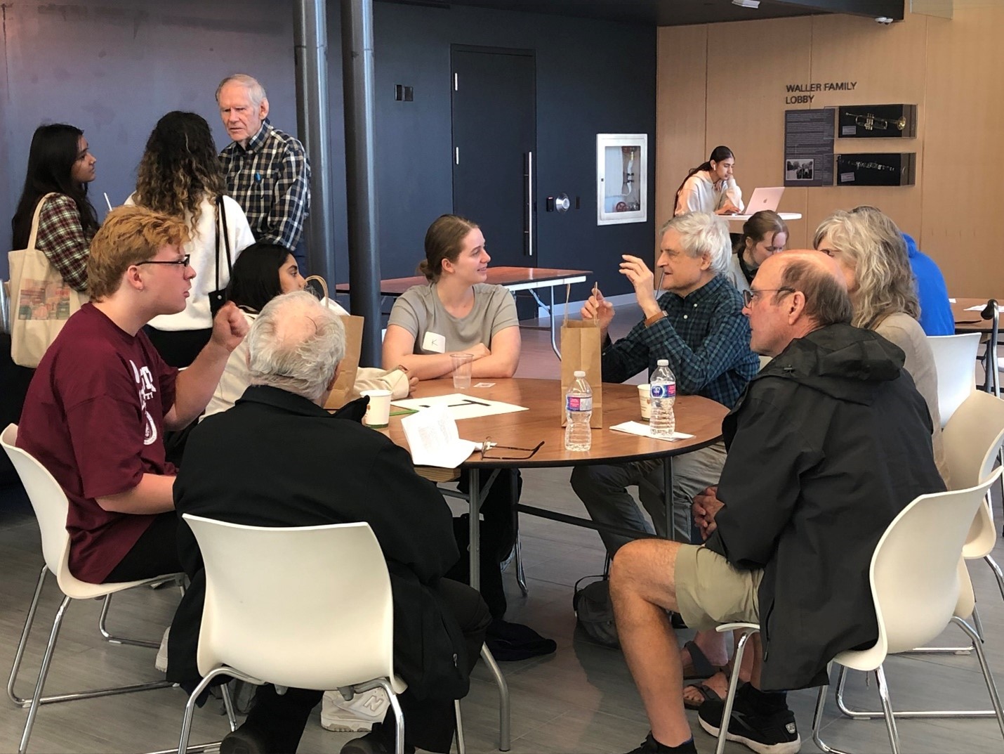 A group of students and older adults mingle at a table.