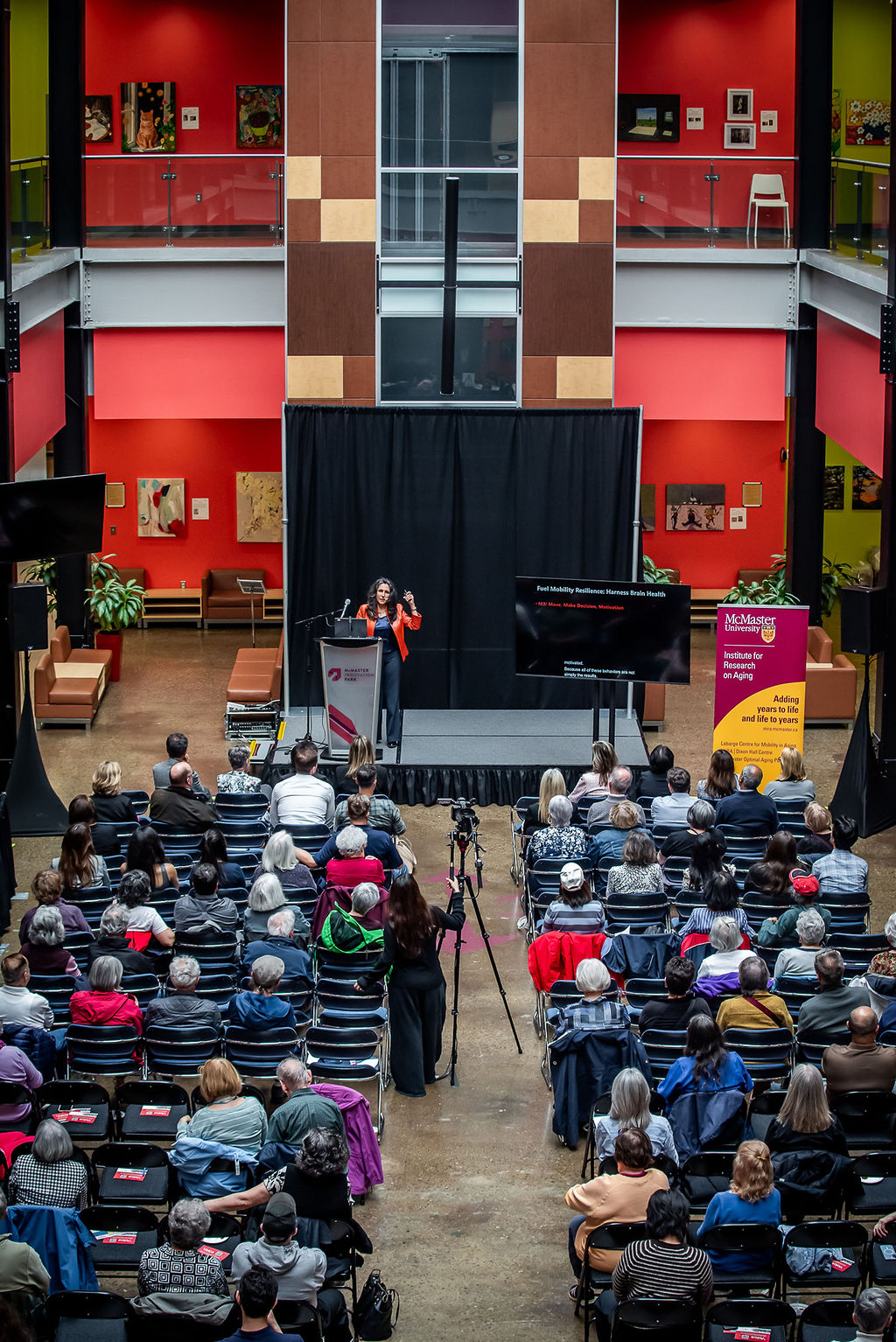 The auditorium of McMaster Innovation Park with people seated in rows of chairs listening to Caterina Rosano speak from a stage