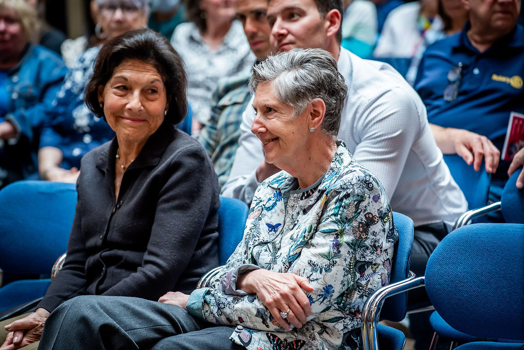 Susan Denburg and Suzanne Labarge sit in the audience of a talk