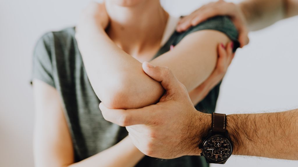 A seated woman has her arm and shoulder assessed